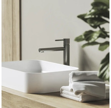 Moderní koupelna s bílým umyvadlem na desku, tmavě šedou baterií na dřevěné desce a bílými ručníky.