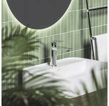 Moderní koupelna s bílým umyvadlem, chromovou baterií, zelenými vertikálními obklady a kulatým zrcadlem.