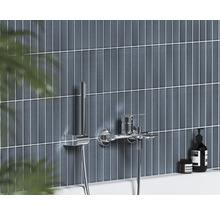 Moderní nástěnná vanová baterie s ruční sprchou v chromu na stěně s tmavě modrými svislými obklady.