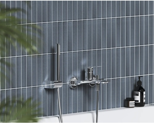 Moderní nástěnná vanová baterie s ruční sprchou v chromu na stěně s tmavě modrými svislými obklady.