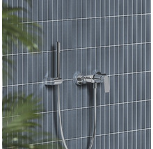 Chromová páková vanová baterie s tyčovou ruční sprchou na moderně obložené stěně.