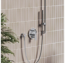 Moderní podomítková sprchová baterie v chromu s pákovým ovládáním, nástěnnou přípojkou a ruční sprchou na tyči před obloženou stěnou.