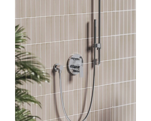 Moderní podomítková sprchová baterie v chromu s pákovým ovládáním, nástěnnou přípojkou a ruční sprchou na tyči před obloženou stěnou.