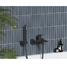 Černá nástěnná vanová baterie s ruční sprchou na vertikálně obložené stěně v moderní koupelně.