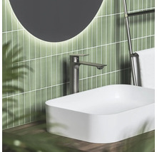 Moderní koupelna s bílým umyvadlem na desku, vysokou tmavou baterií a zeleným vertikálním obkladem.