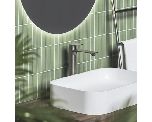 Moderní koupelna s bílým umyvadlem na desku, vysokou tmavou baterií a zeleným vertikálním obkladem.