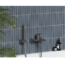 Nástěnná vanová baterie s ruční sprchou v tmavém kovovém provedení na vertikálně obložené stěně.