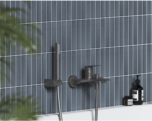 Nástěnná vanová baterie s ruční sprchou v tmavém kovovém provedení na vertikálně obložené stěně.