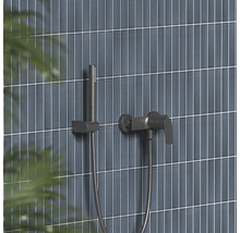 Moderní sprchová baterie a tyčová ruční sprcha v tmavém kovovém vzhledu na stěně s úzkými vertikálními obklady.