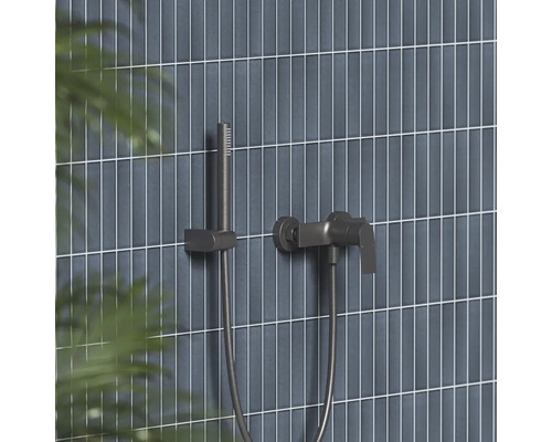 Moderní sprchová baterie a tyčová ruční sprcha v tmavém kovovém vzhledu na stěně s úzkými vertikálními obklady.