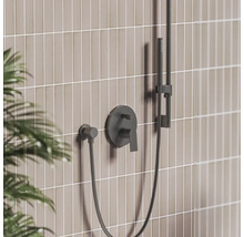 Černá podomítková sprchová baterie s pákou, ruční sprchou na tyči a hadicí před dlážděnou stěnou.