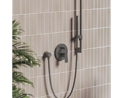 Černá podomítková sprchová baterie s pákou, ruční sprchou na tyči a hadicí před dlážděnou stěnou.