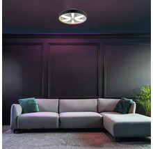 Moderní LED stropní svítidlo s ventilátorem a funkcí barev RGB, namontované v tmavém obývacím pokoji s šedou pohovkou a nástěnnými panely.