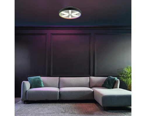 Moderní LED stropní svítidlo s ventilátorem a funkcí barev RGB, namontované v tmavém obývacím pokoji s šedou pohovkou a nástěnnými panely.