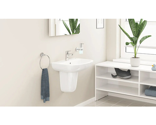 Moderní koupelna s bílým nástěnným umyvadlem s polosloupem, chromovou baterií, dávkovačem mýdla, kruhem na ručník a policí.