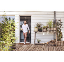 Muž prochází magnetickým závěsem proti hmyzu u terasových dveří na dřevěnou terasu s mnoha rostlinami v květináčích.