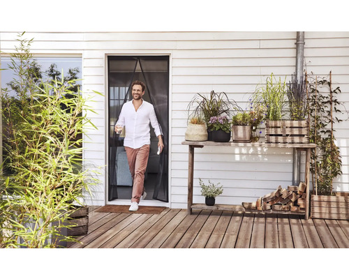 Muž prochází magnetickým závěsem proti hmyzu u terasových dveří na dřevěnou terasu s mnoha rostlinami v květináčích.