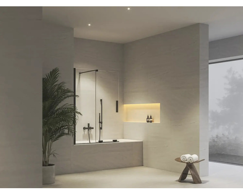 Moderní světlá koupelna se skleněnou sprchovou zástěnou na vaně, armaturami, pokojovou rostlinou a osvětleným výklenkem.