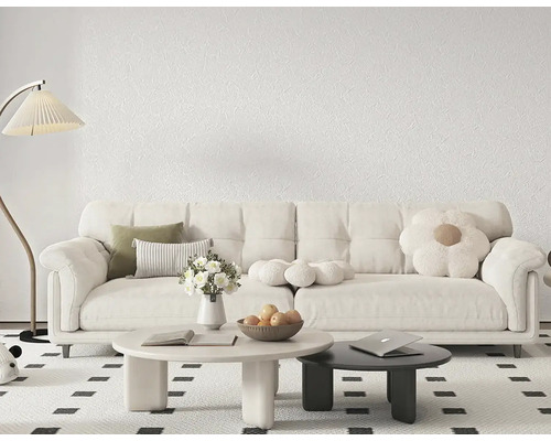 Moderní obývací pokoj s bílou strukturovanou tapetou, velkou pohovkou, kulatými stolky a stojací lampou na vzorovaném koberci.