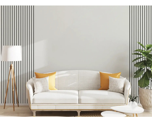 Moderní obývací pokoj s bílou pohovkou, žlutými polštáři, dřevěnou stojací lampou a nástěnnou dekorací s černými svislými pruhy.