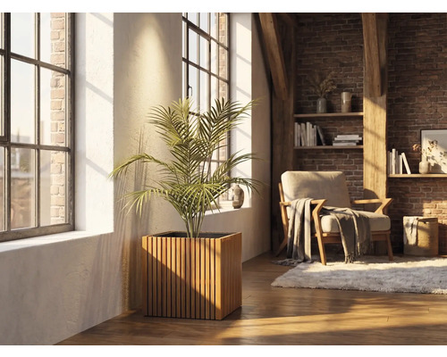 Čtvercový dřevěný květináč s vertikálními lamelami a pokojovou rostlinou ve světlém obývacím pokoji s cihlovou stěnou a velkými okny.