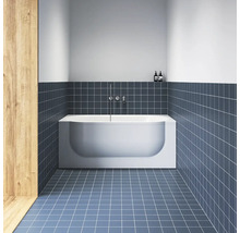 Moderní koupelna s bílou obdélníkovou vanou, modrými čtvercovými dlaždicemi na podlaze i stěnách a chromovanou nástěnnou baterií.