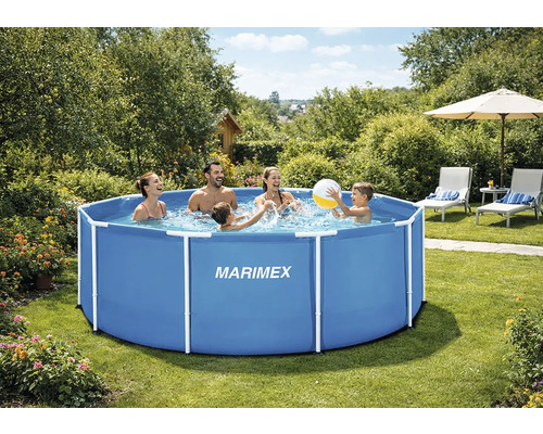 Rodina si hraje s míčem v kulatém modrém bazénu s rámem Marimex ve světlé, bujné zahradě s lehátky.