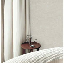 Světlá strukturovaná vliesová tapeta ve světlém obývacím pokoji s bílým závěsem a kulatým dřevěným stolkem.