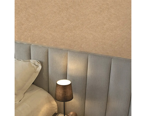 Strukturovaná béžová tapeta nad šedým čalouněným čelem postele v ložnici s rozsvícenou noční lampou.