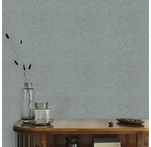 Strukturovaná vliesová tapeta v modrošedé barvě na stěně za dřevěnou komodou se skleněnými vázami a sušenými rostlinami.