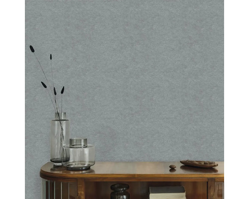 Strukturovaná vliesová tapeta v modrošedé barvě na stěně za dřevěnou komodou se skleněnými vázami a sušenými rostlinami.