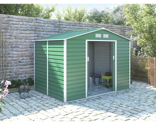 Zelený kovový zahradní domek se sedlovou střechou a posuvnými dveřmi na dlážděné terase u cihlové zdi.