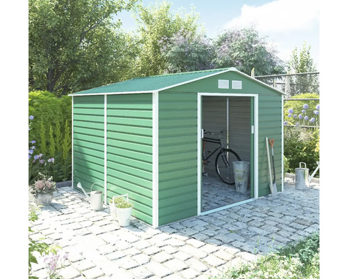 Zelený kovový zahradní domek se sedlovou střechou a posuvnými dveřmi na dlažbě v zahradě, s jízdním kolem uvnitř a zahradním nářadím venku.