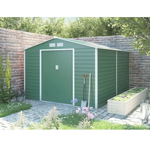 Zelený kovový zahradní domek se sedlovou střechou a bílým rámem v zahradě před cihlovou zdí.