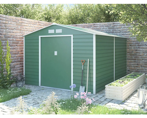 Zelený kovový zahradní domek se sedlovou střechou a bílým rámem v zahradě před cihlovou zdí.