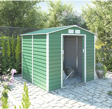 Zelený kovový zahradní domek se sedlovou střechou a bílým rámem, posuvnými dveřmi a ventilací, na kamenné dlažbě ve světlé zahradě.