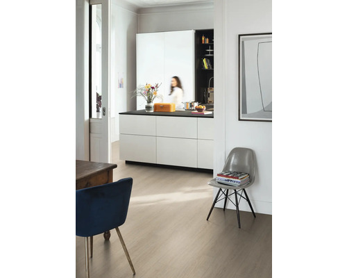 Moderní světlý pokoj s laminátovou podlahou ve světlém dekoru dřeva, bílým kuchyňským ostrůvkem s černou pracovní deskou a designovými židlemi.