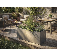 Velký obdélníkový květináč v betonovém vzhledu na dřevěné terase v moderně navržené zahradě s posezením a ohništěm.
