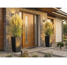 Moderní vchod do domu s dřevěnými dveřmi, kamenným obkladem a dvěma vysokými květináči v ratanovém vzhledu s pampovou trávou.