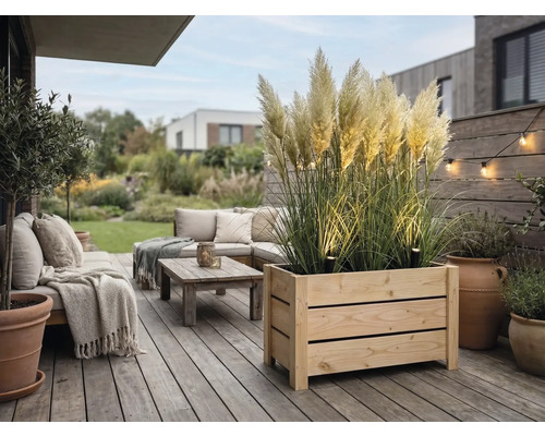 Moderní dřevěná terasa s velkým truhlíkem s pampovou trávou, venkovním nábytkem s polštáři, stolkem a dekorativním osvětlením.