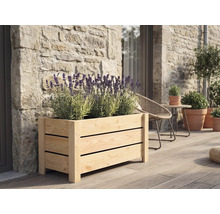 Obdélníkový dřevěný truhlík s lamelami s kvetoucí levandulí na dřevěné terase u kamenné zdi.