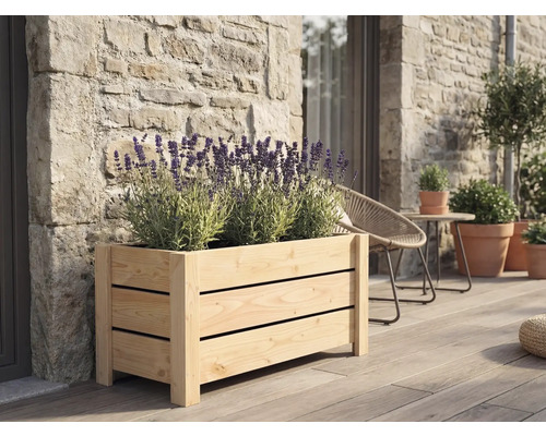 Obdélníkový dřevěný truhlík s lamelami s kvetoucí levandulí na dřevěné terase u kamenné zdi.