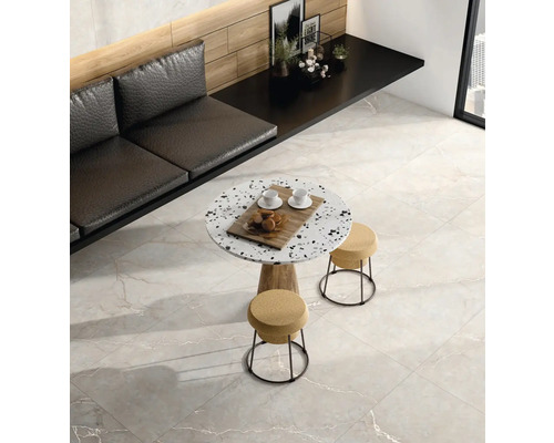 Moderní místnost se světle šedou dlažbou v dekoru mramoru, kulatým terazzo stolem se stoličkami a černou lavicí u dřevěné stěny.