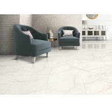 Světlý obývací pokoj se dvěma modrými křesly na velkoformátové dlažbě s mramorovým efektem a hnědým žilkováním u bílé cihlové stěny.