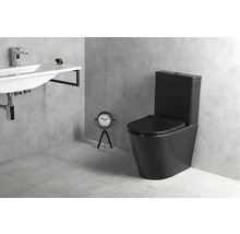 Moderní koupelna s černým stojícím WC s nádržkou, bílým nástěnným umyvadlem s chromovou baterií a šedou dlažbou v betonovém vzhledu.