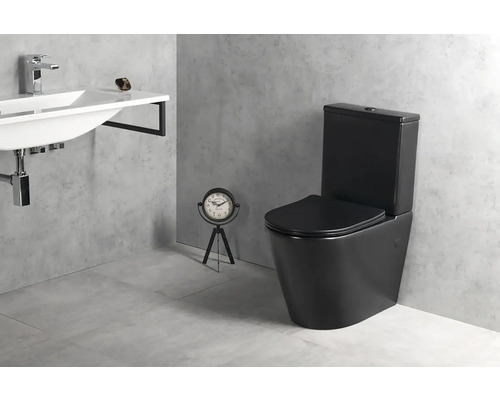 Moderní koupelna s černým stojícím WC s nádržkou, bílým nástěnným umyvadlem s chromovou baterií a šedou dlažbou v betonovém vzhledu.