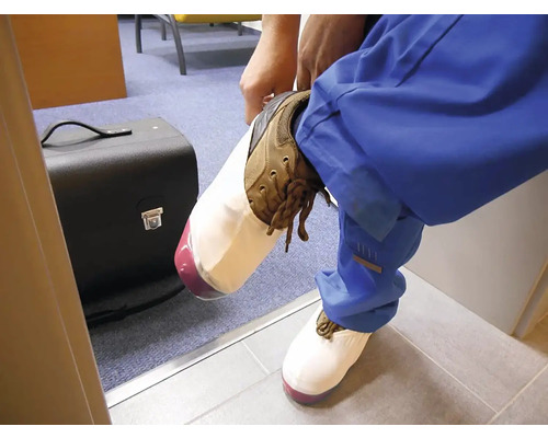 Osoba si navléká bílé návleky na pracovní boty, aby chránila podlahové krytiny před nečistotami.