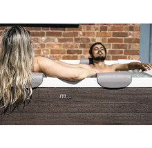 Muž a žena relaxují ve vířivce MSpa s vnějším obložením v dekoru dřeva před cihlovou zdí.