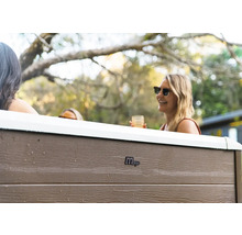 Venkovní pohled na vířivku MSpa s panely v dekoru dřeva a osobami na zahradě.