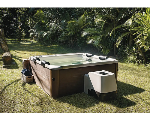 Čtvercová vířivka s obložením v dekoru dřeva a externí čerpací jednotkou, na trávníku v zahradě s palmami.